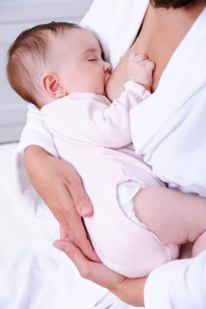 Little beautiful newborn baby eating milk from mother's breast